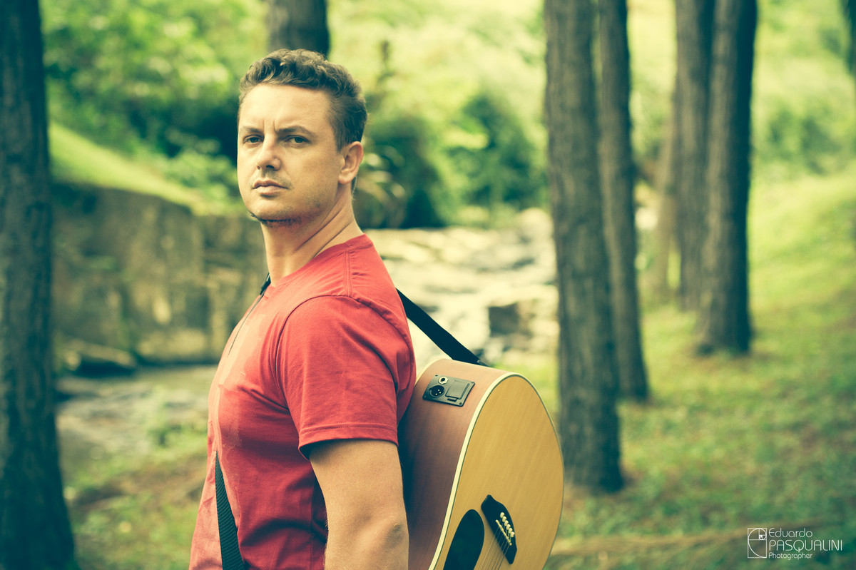 Homem com violão acústico nas costas em meio a natureza. Foto de Eduardo Pasqualini, fotógrafo de casamentos e ensaios em Rio do Sul, Santa Catarina.