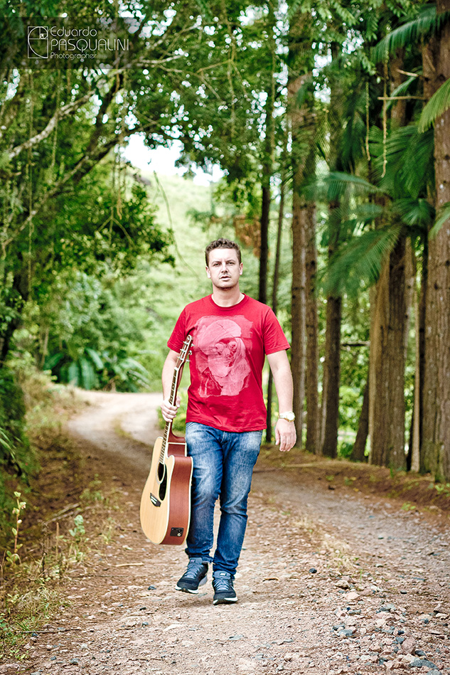 Caminhando e segurando violão em uma estrada de chão. Foto de Eduardo Pasqualini, fotógrafo de casamentos e ensaios em Rio do Sul, Santa Catarina.