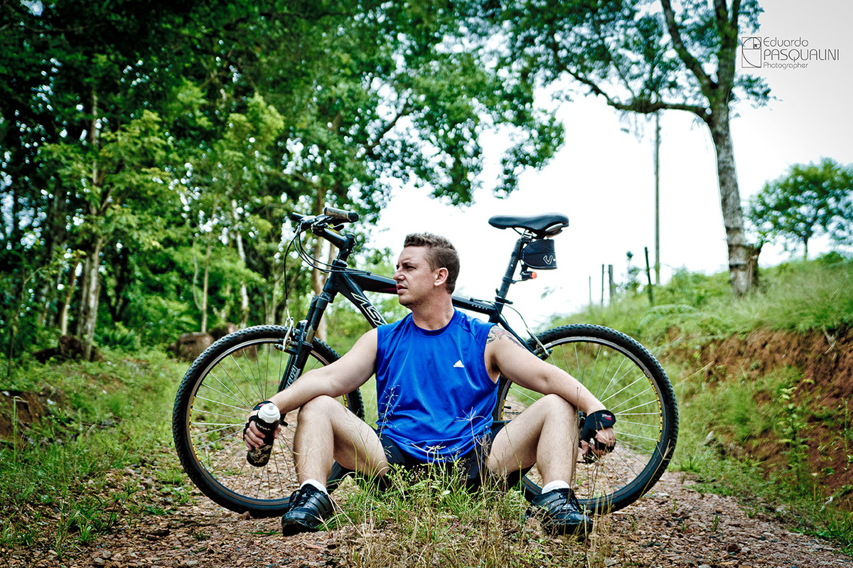 Sentado junto a bicicleta moutain bike em estrada de terra. Foto de Eduardo Pasqualini, fotógrafo de casamentos e ensaios em Rio do Sul, Santa Catarina.