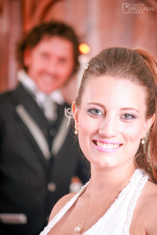 Noiva Ester, olhar fixo para a Câmera e noivo Fernando ao fundo. Fotografia de Eduardo Pasqualini, fotógrafo de casamentos e ensaios em Rio do Sul, Santa Catarina.