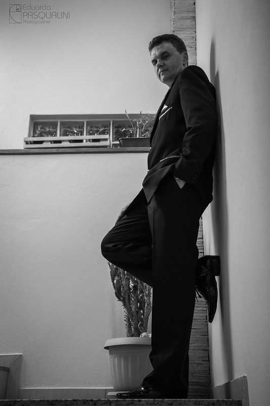 Noivo encostado em parede branca junto a escada no dia do casamento. Fotografia de Eduardo Pasqualini, fotógrafo de casamentos e ensaios em Rio do Sul, Santa Catarina.