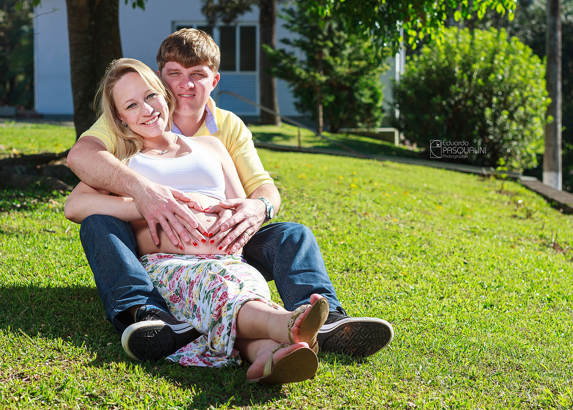 Casal gestante abraçados em gramado. Fotografia de Eduardo Pasqualini, fotógrafo de casamentos e ensaios em Rio do Sul, Santa Catarina.