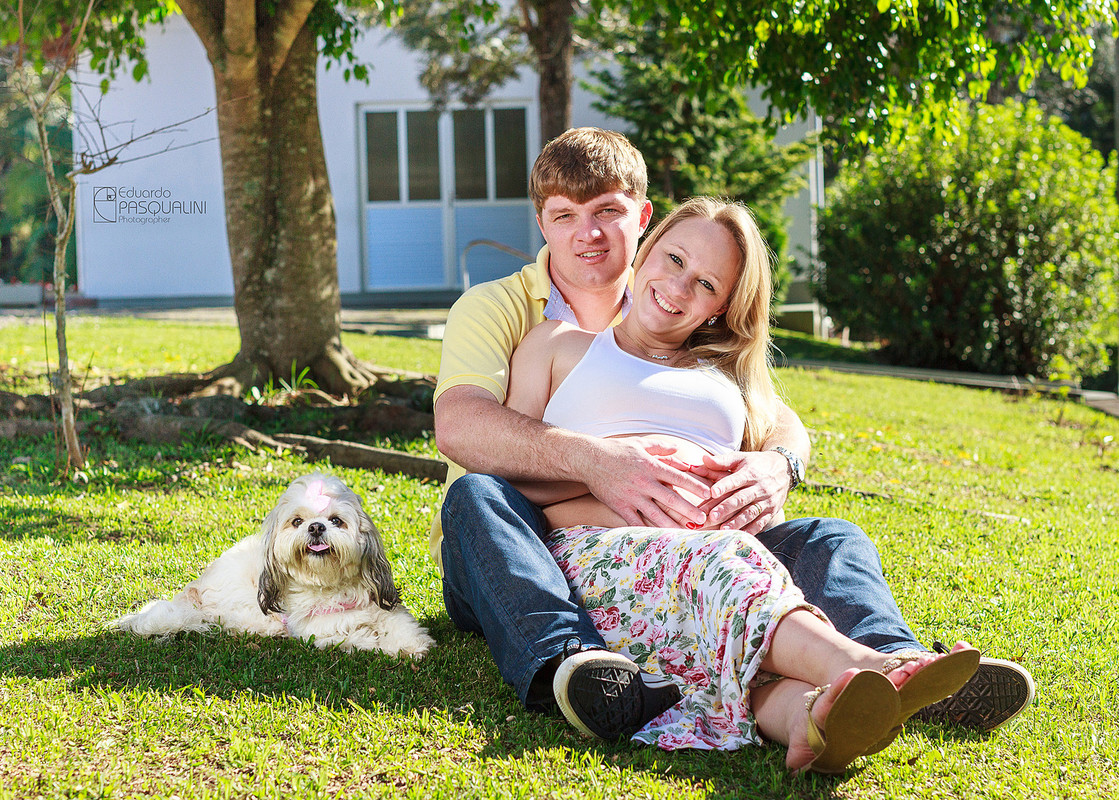 Gestantes e cachorrinho lhasa apso em gramado verde. Fotografia de Eduardo Pasqualini, fotógrafo de casamentos e ensaios em Rio do Sul, Santa Catarina.