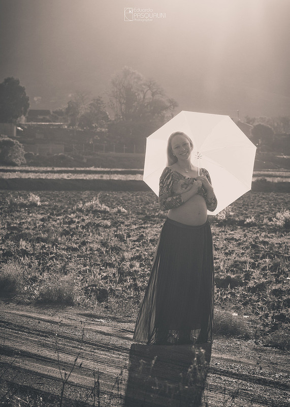 Gestante segurando sombrinha branca em foto preto e branca. Fotografia de Eduardo Pasqualini, fotógrafo de casamentos e ensaios em Rio do Sul, Santa Catarina.