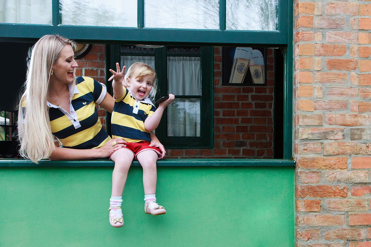 Criança linda brincando com a mãe em janela verde. Fotografia de Eduardo Pasqualini, fotógrafo de casamentos e ensaios em Rio do Sul, Santa Catarina.