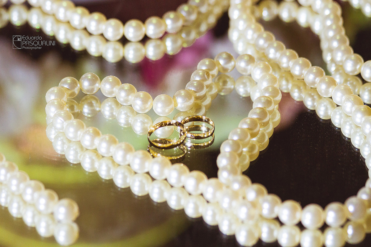 As alianças do casamento junto a pérolas em formato de coração. Fotografia de Eduardo Pasqualini, fotógrafo de casamentos e ensaios em Rio do Sul, Santa Catarina.