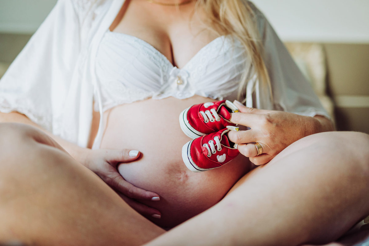 Mamãe com sapatinhos do bebê. Ensaio de gestante em casa. Fotografia de Eduardo Pasqualini, fotógrafo de casamentos e ensaios em Rio do Sul, Santa Catarina.
