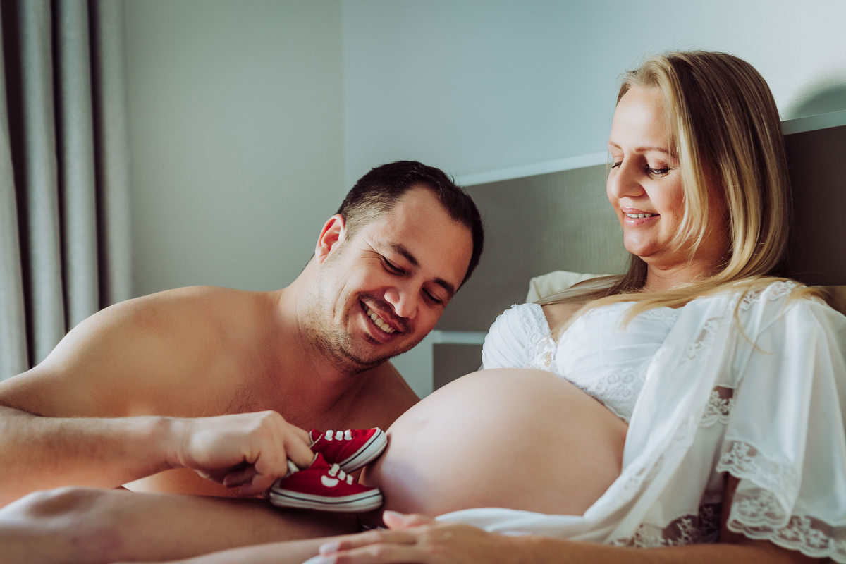 Papai brincando na barriga da futura mamãe. Ensaio de gestante em casa. Fotografia de Eduardo Pasqualini, fotógrafo de casamentos e ensaios em Rio do Sul, Santa Catarina.