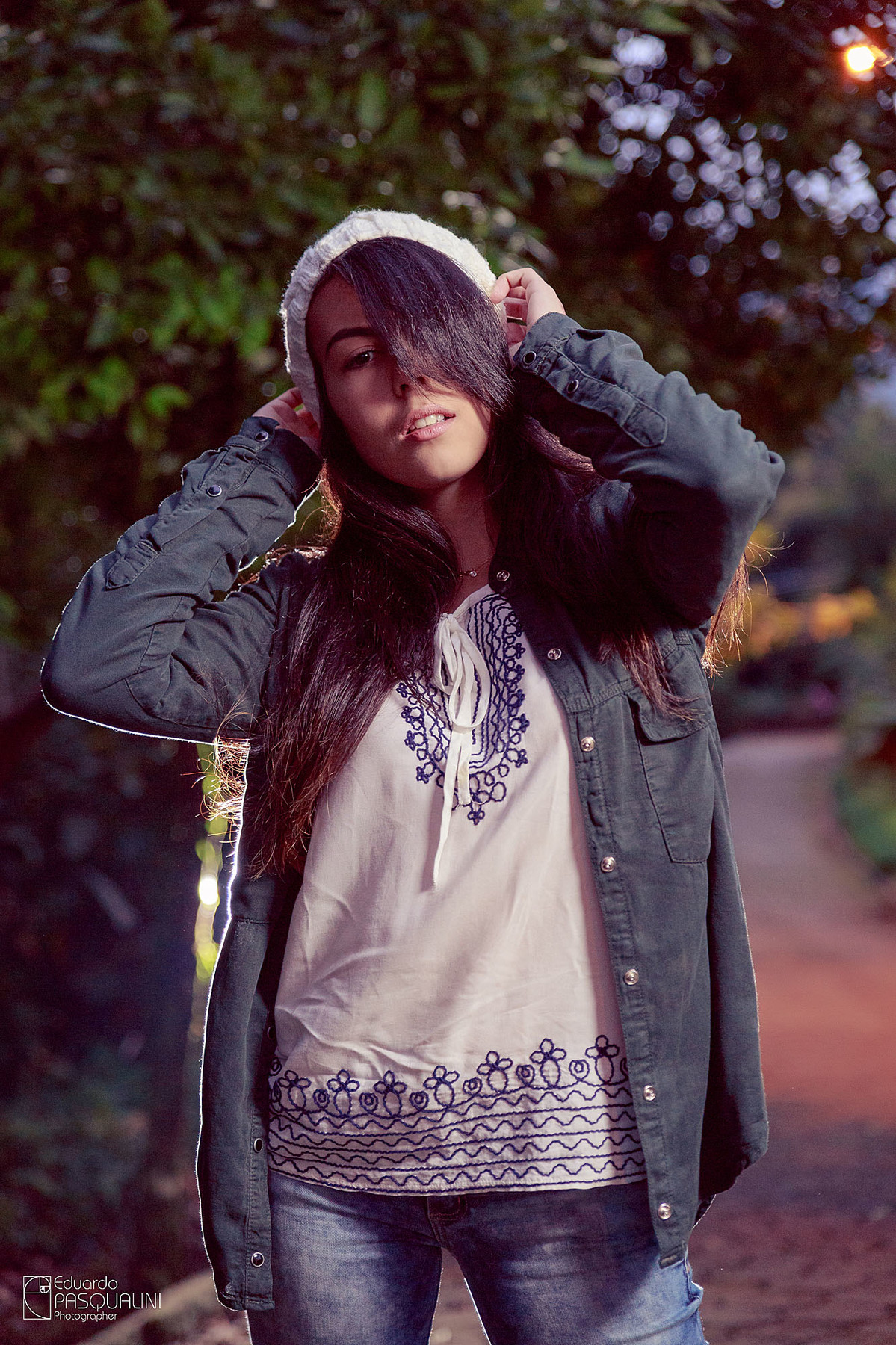Segurando gorro, modelo em pé vestindo blusa branca e jaqueta. Fotografia de Eduardo Pasqualini, fotógrafo de casamentos e ensaios em Rio do Sul, Santa Catarina.