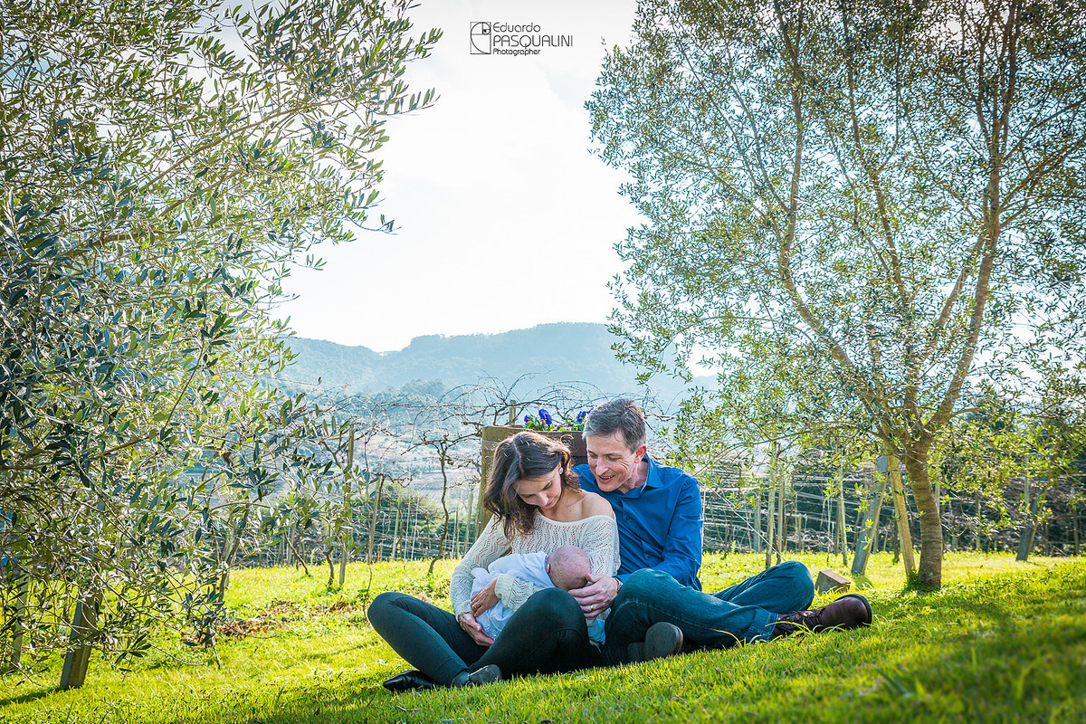 Em meio a natureza, família de pai, mãe e bebê sentados na grama. Osteria La Campagnaga. Fotografia de Eduardo Pasqualini, fotógrafo de casamentos e ensaios em Rio do Sul, Santa Catarina.
