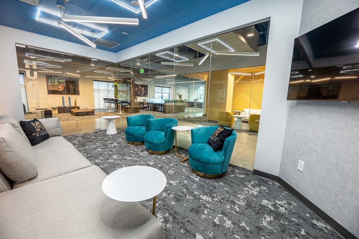 Contemporary office interior in Orlando, FL, ideal for interior and real estate photography. Features vibrant blue armchairs, gray sofa, and a workspace visible through glass walls, perfect for professional portfolios.