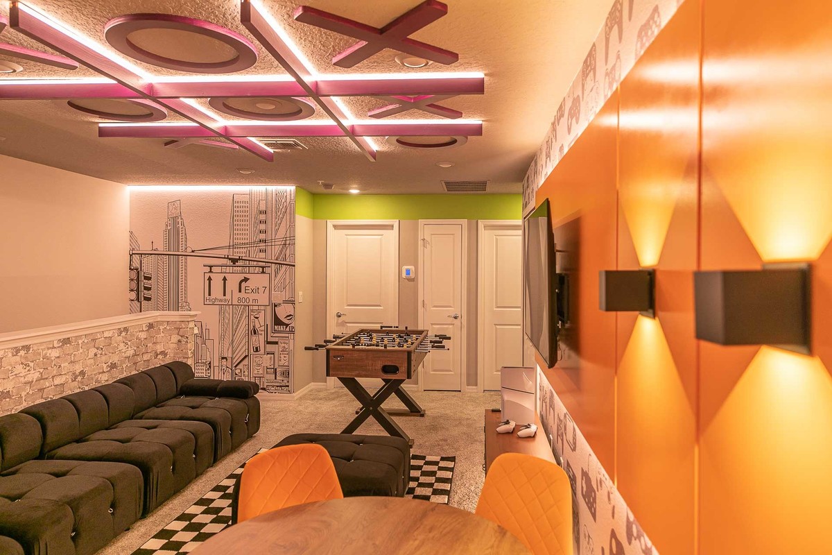 The second image features a game room with a foosball table, checkered carpet, orange and black accents, and a ceiling with geometric lighting. Real Estate and Interior Photography by Magic Lens Photo Media.