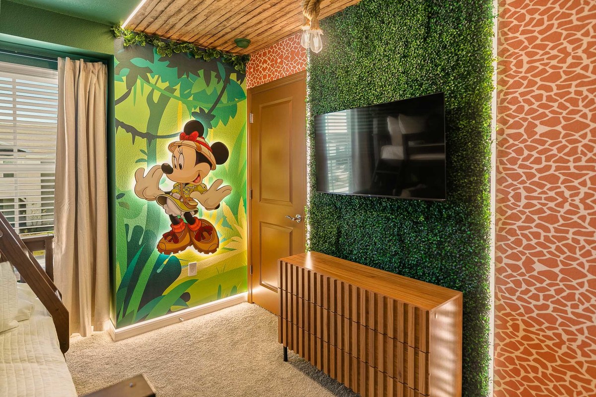 The first image shows a Mickey Mouse
 jungle-themed room with a cartoon mural, a leafy green wall, and a TV, creating a lively, nature-inspired space. Real Estate and Interior Photography by Magic Lens Photo Media.