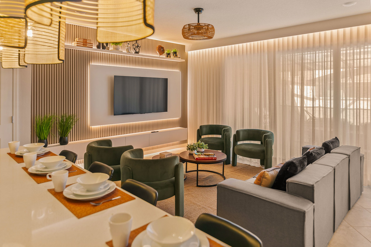 Living area with green armchairs facing an entertainment wall with LED lighting. Kitchen counter with matching pendant lights adds cohesion to the open layout. Real Estate and Interior Photography by Magic Lens Photo Media.