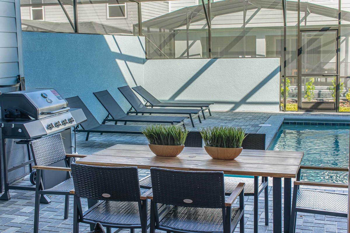 Outdoor area with a wooden table, barbecue, and a beautiful pool. Real Estate and Interior Photography by Magic Lens Photo Media.