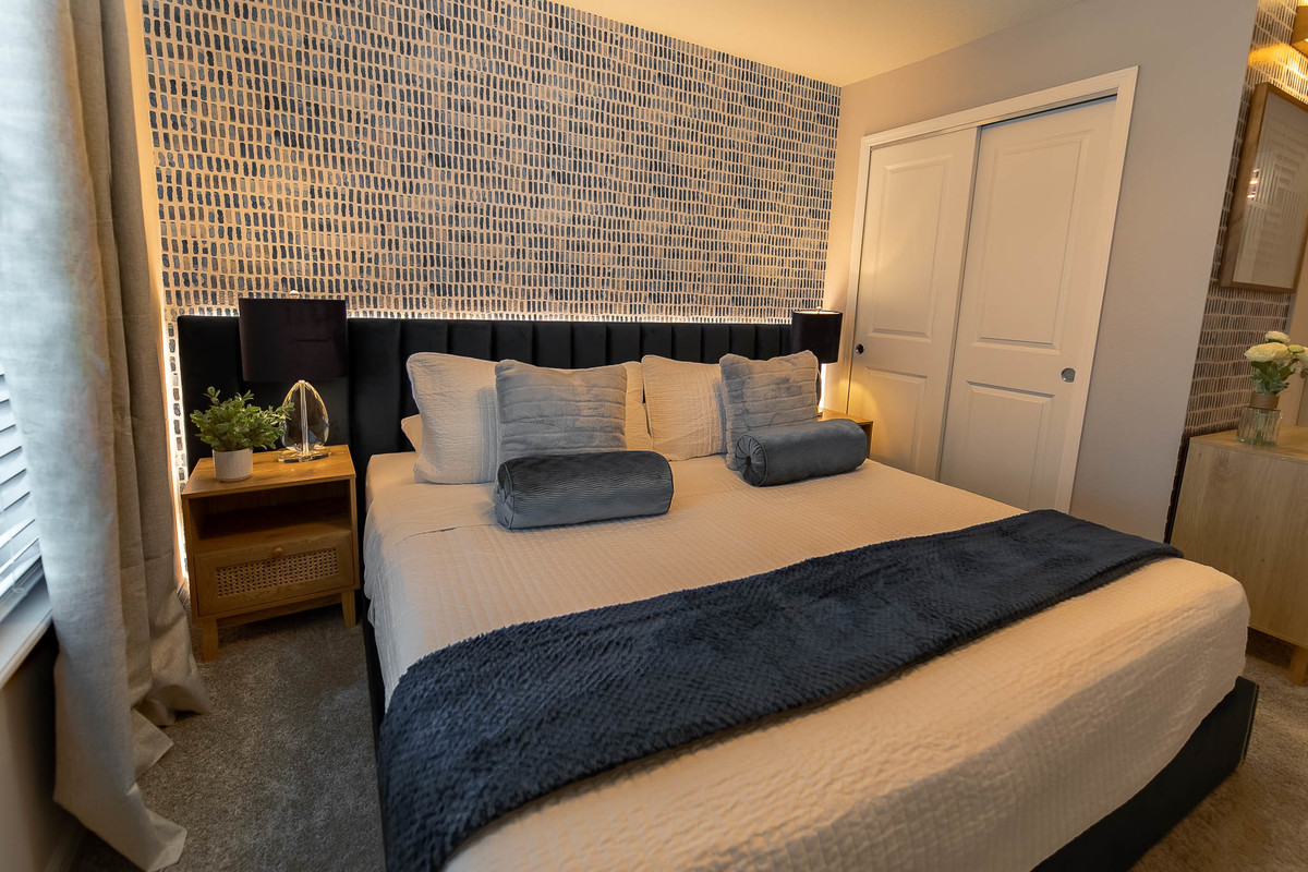 Modern bedroom with textured wall, dark blue decor, and simple nightstands with lamps. Real Estate and Interior Photography by Magic Lens Photo Media.