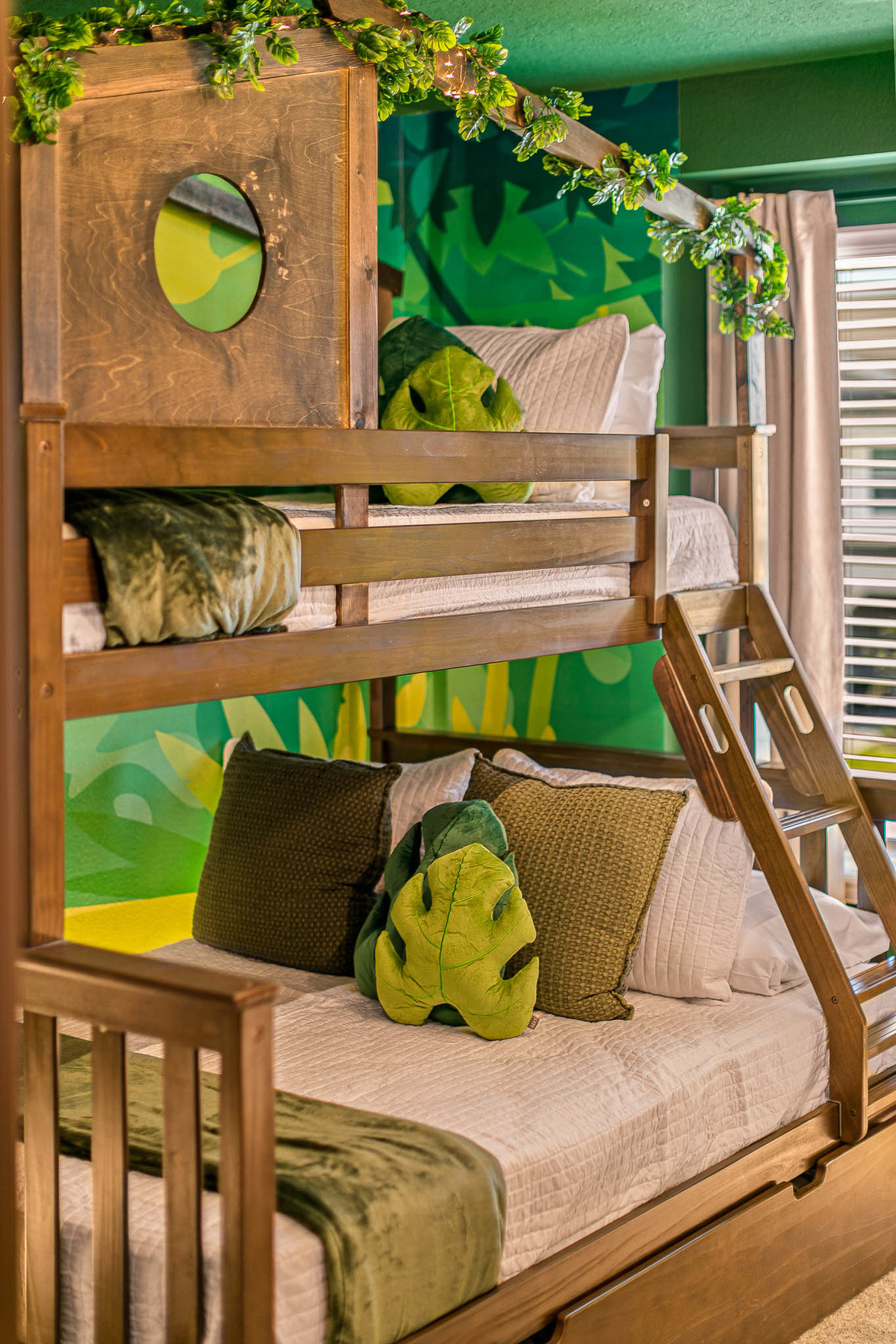 Jungle-themed bunk bed room with green leafy decor, wood frames, and nature-inspired pillows. Real Estate and Interior Photography by Magic Lens Photo Media.