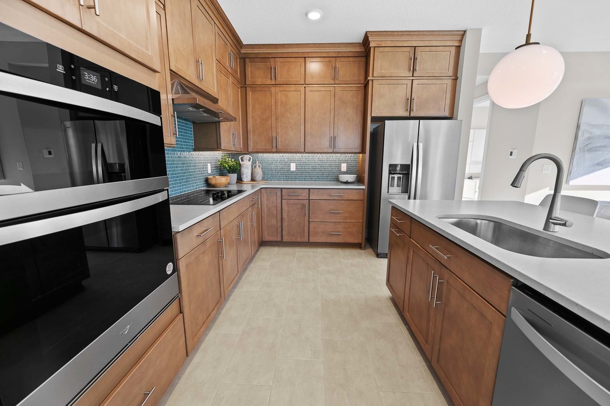 Spacious luxury kitchen featuring rich brown wood cabinetry, a sleek central island with ample seating, and premium stainless steel appliances. Perfect for modern living and entertaining. Luxury Reals Estate Photography by Magic Lens Photo Media in Orland
