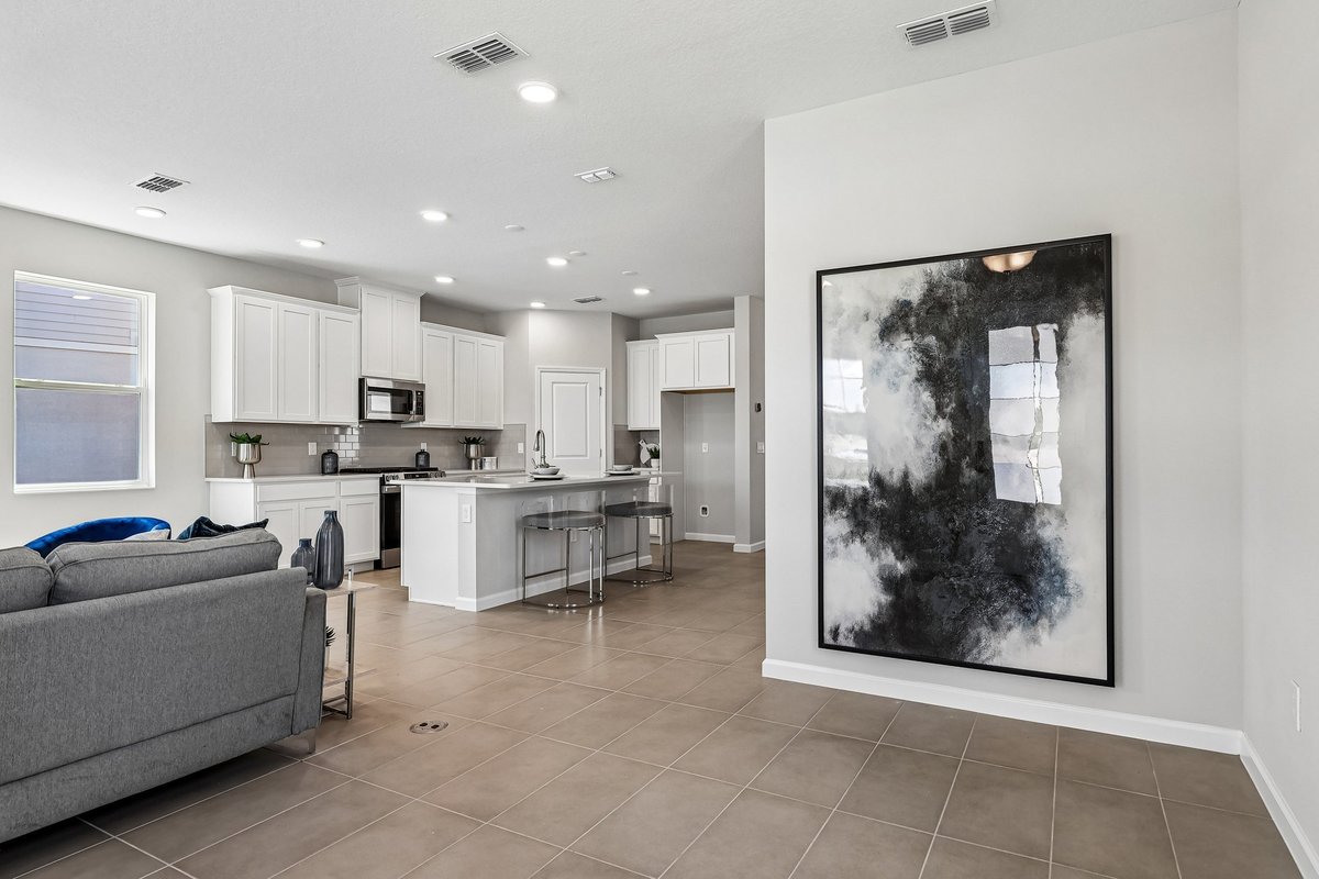 open-concept-living-room-kitchen-white-cabinets-gray-sofa-modern-abstract-art-tile-floor-5348-ctr-lk-rnch-blvd-st-cloud-fl