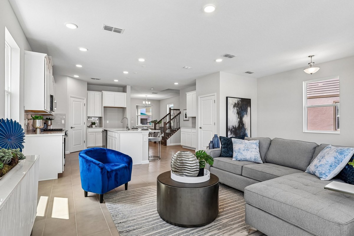 spacious-open-floor-plan-living-area-gray-sectional-blue-velvet-accent-chair-white-kitchen-staircase-5348-ctr-lk-rnch-blvd-st-cloud-fl
