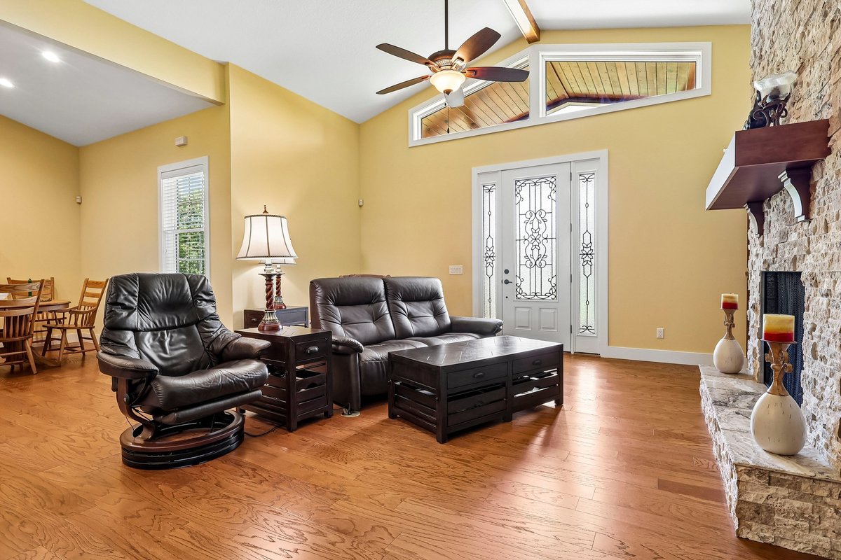 Open living room with wood floors, high ceilings, fireplace, and leather seating in Haines City home