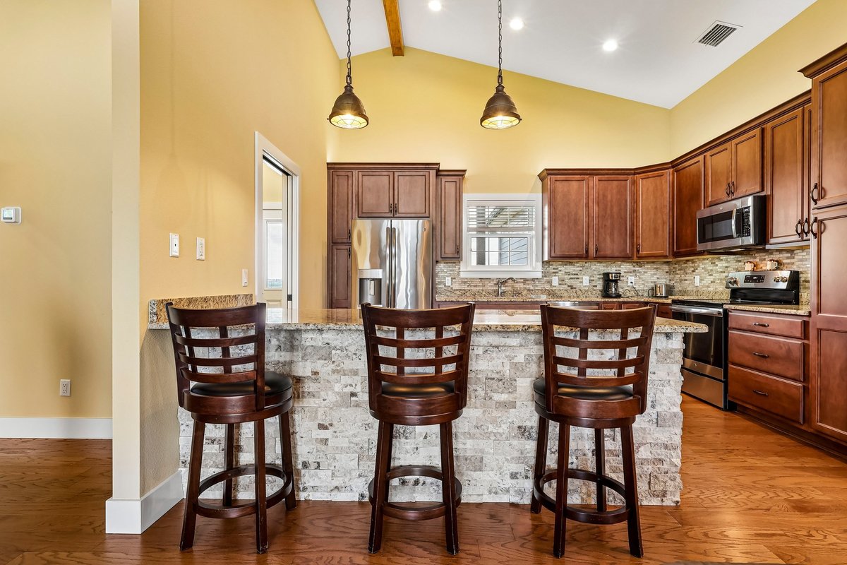 Kitchen bar seating with stone island, wood cabinetry, pendant lights, and open living area