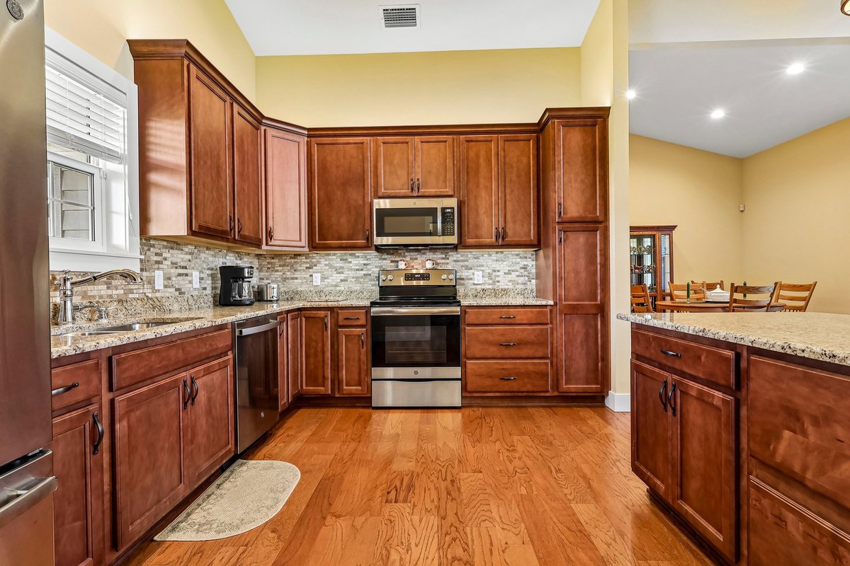 Kitchen with solid wood cabinets, stone countertops, stainless steel appliances, and wood floors