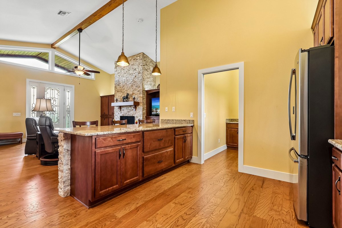 Kitchen island view into open living room with fireplace, wood floors, and vaulted ceiling