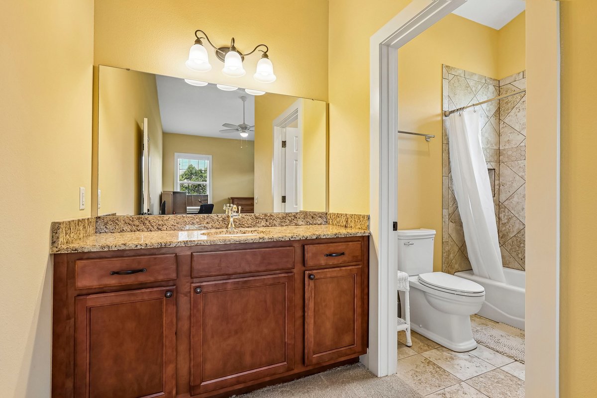 Bathroom with wood vanity, large mirror, stone countertop, and tub shower