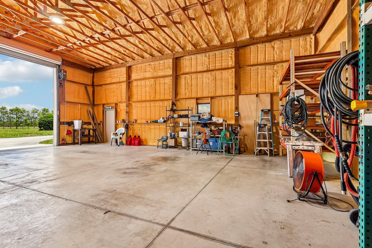 Interior view of a large insulated workshop with concrete floors, storage racks, tools, and an open garage door on a rural Haines City property.