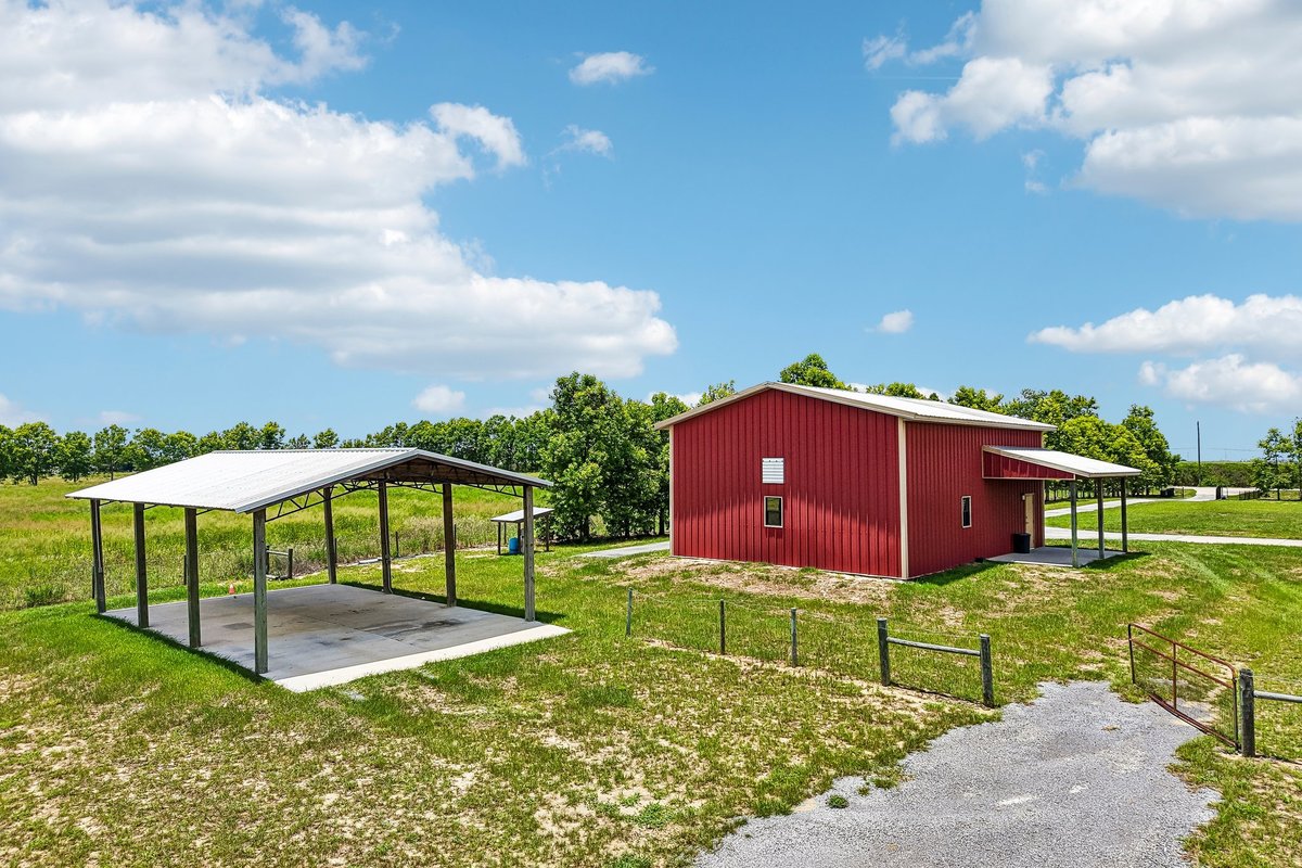 Side exterior of Haines City acreage home with lawn, covered porch, and red workshop nearby