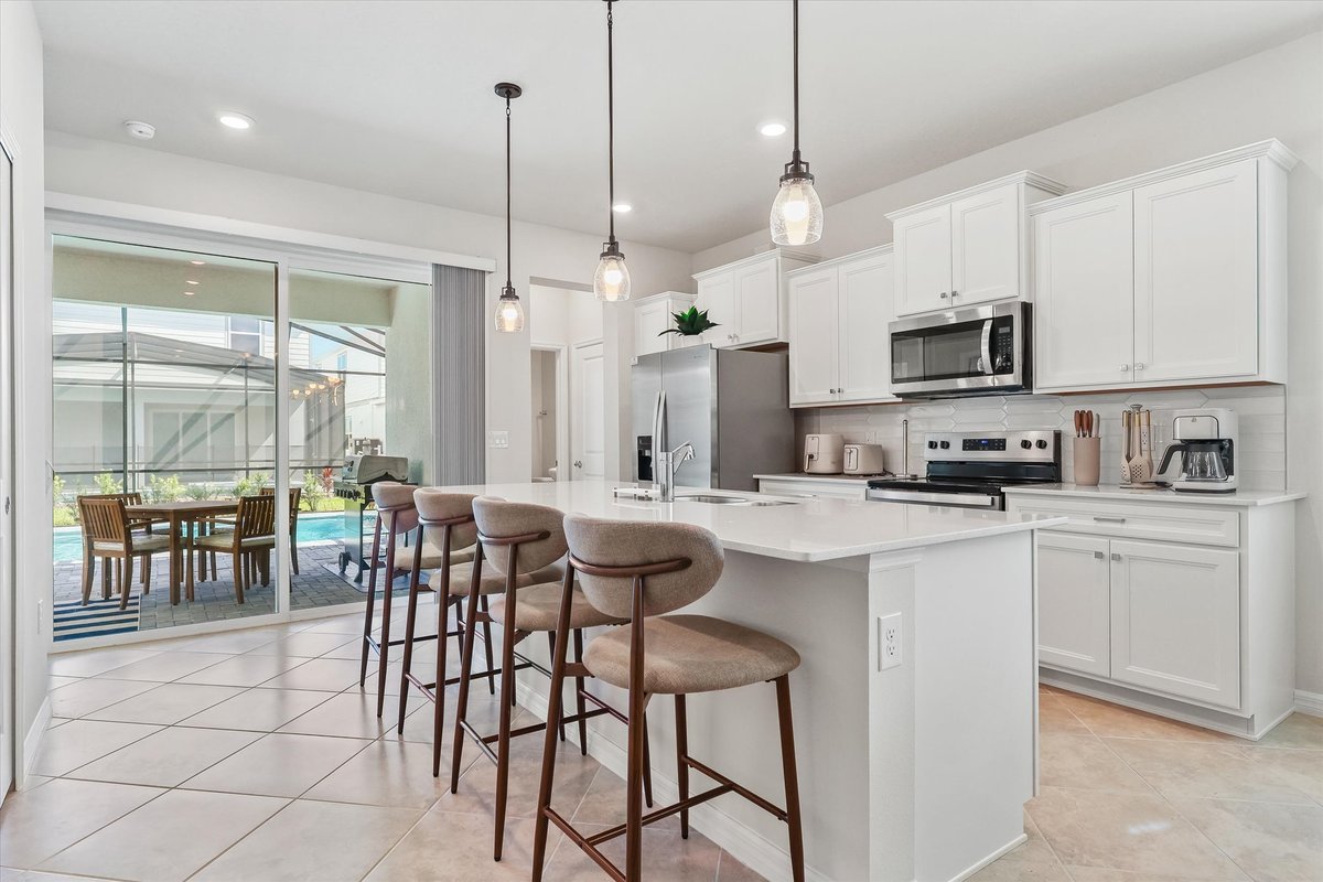 White kitchen with large island, bar seating, stainless appliances and direct access to the covered patio.