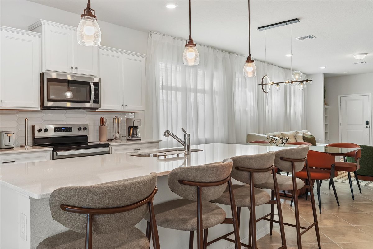 Kitchen island detail with pendant lighting, bar stools and a clean white finish in the open living space.