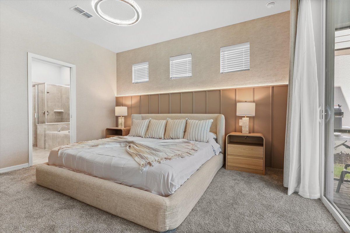 Neutral primary bedroom suite with upholstered bed, warm accent wall, soft lighting and large windows.