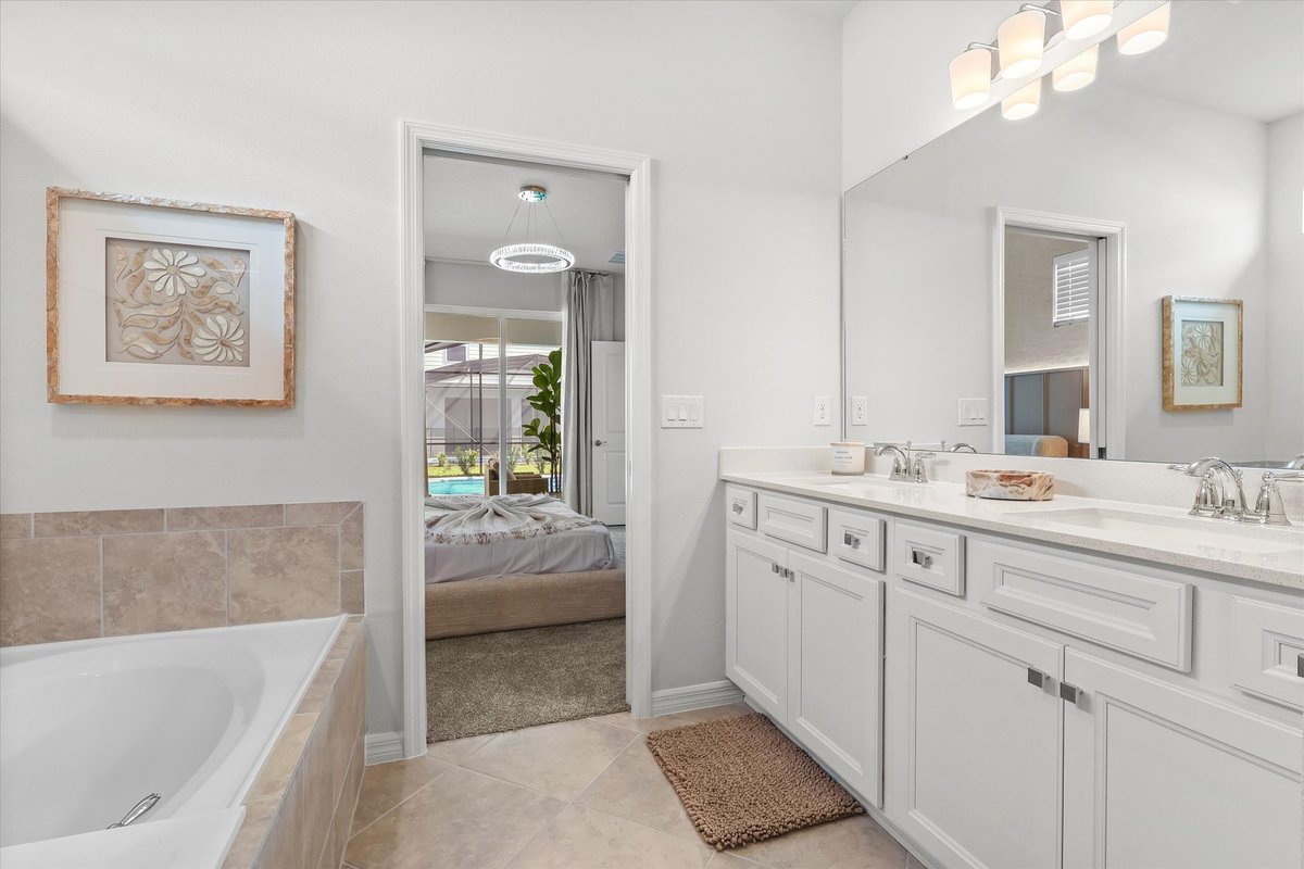 Bright ensuite bathroom with double vanity, large mirror, soaking tub and view into the primary bedroom.