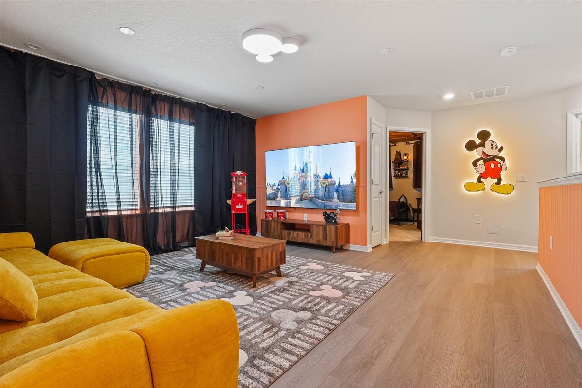 Mickey-themed upstairs lounge with mustard sectional, TV wall and bright orange accent details.