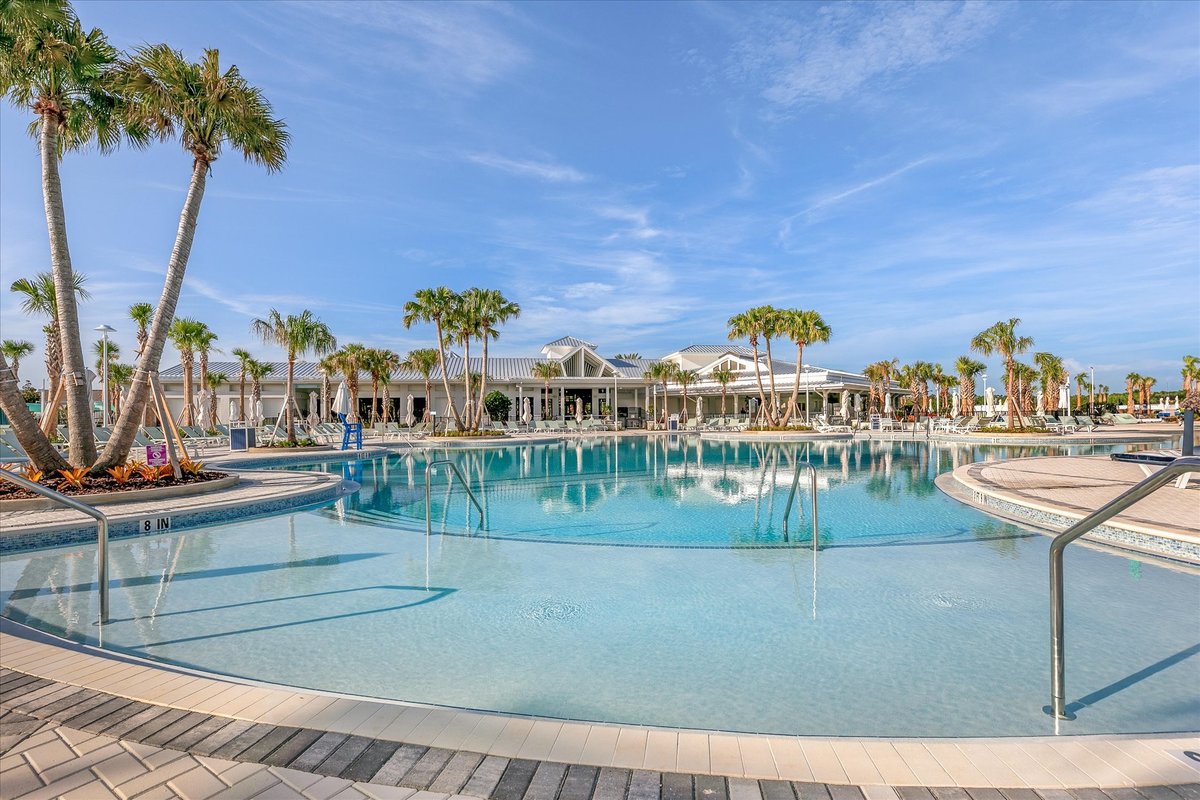 Large resort-style swimming pool at Windsor Cay with palm trees, lounge areas and blue Florida sky.