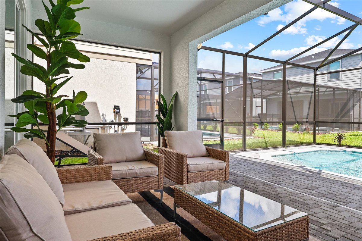 Covered outdoor lounge overlooking the screened private pool, with wicker seating and modern landscaping.