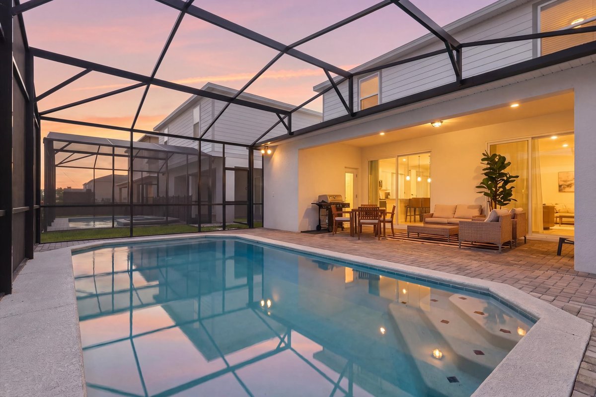 Virtual twilight view of the screened private pool and covered patio with warm evening interior lighting.