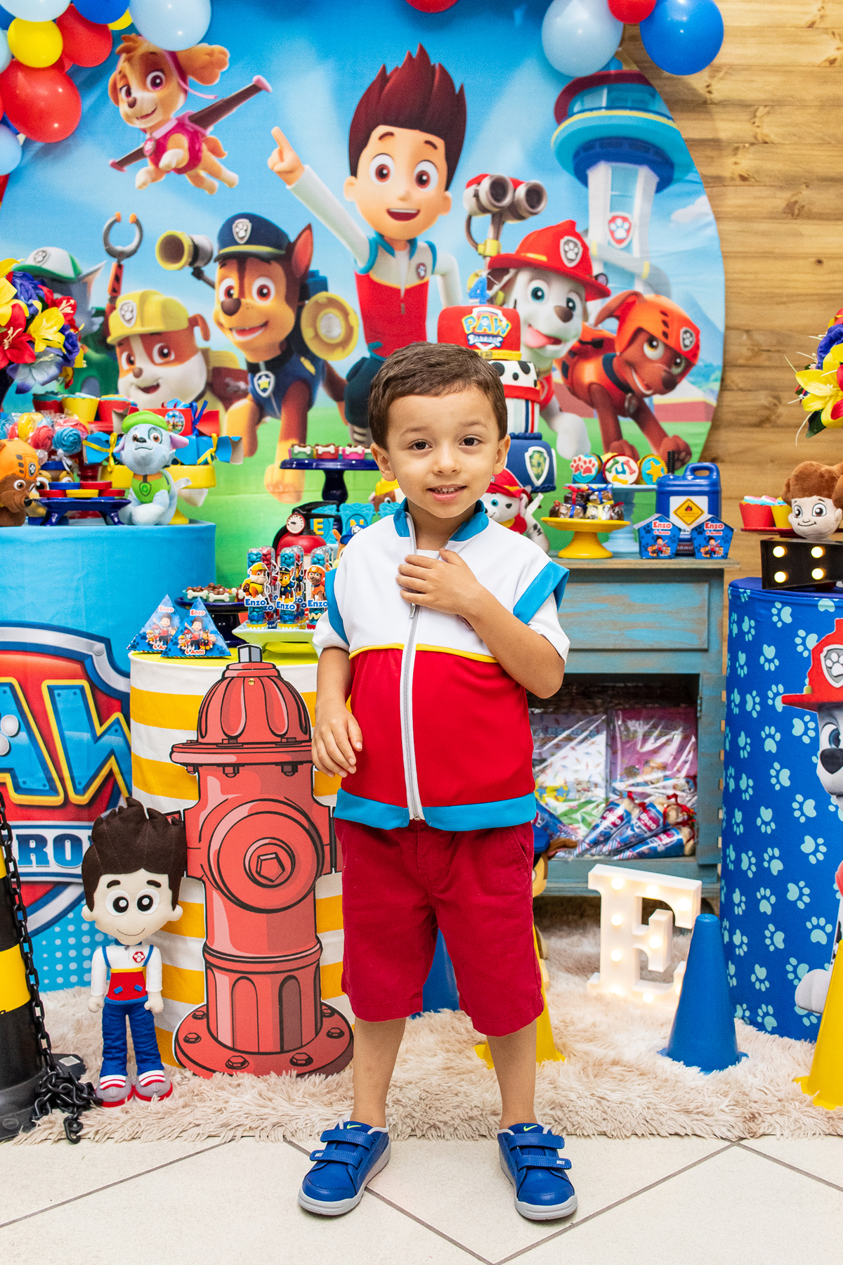 Fotografia do aniversariante em frente à mesa do bolo.