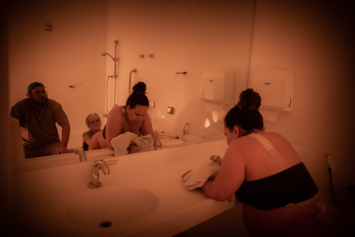 mulher em trabalho de parto sendo observada por seu marido atraves do espelho