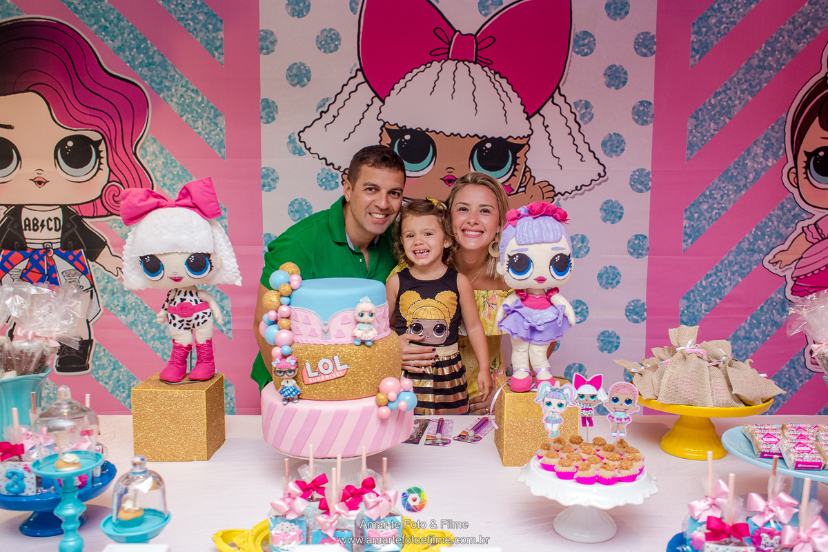 menina de 3 anos vestida de queen b em sua festa de aniversário do tema lol e sorrindo com a mãe e o pai