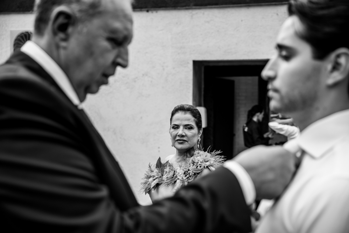 Pai do noivo ajeita sua gravata enquanto a mãe do noivo os observa