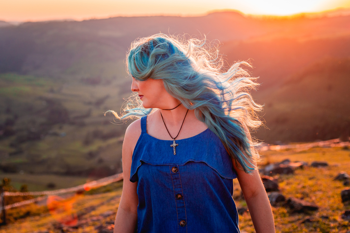 mulher jogando cabelo azul no por do sol para foto em ensaio fotográfico morro do gavião no paraná pelo fotógrafo joão barral