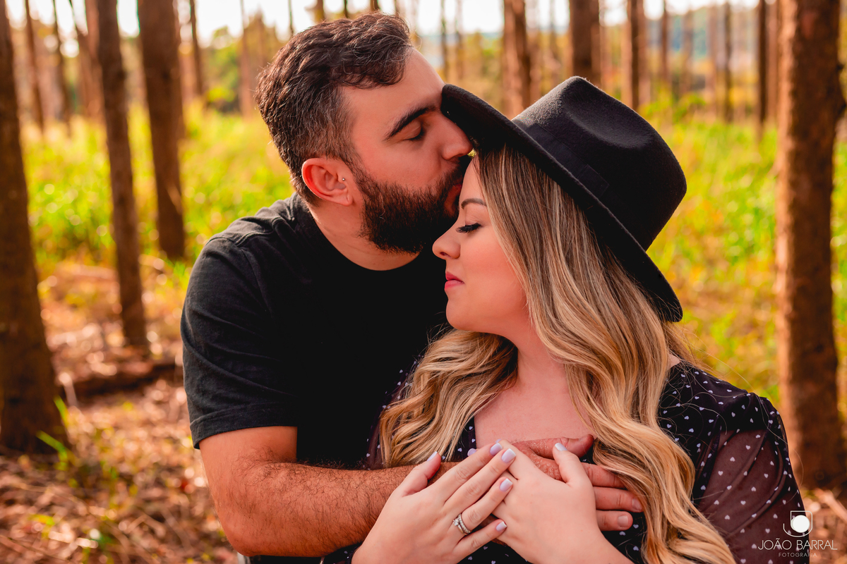 homem dando beijo na testa de mulher gestante com chapéu em ensaio no campo