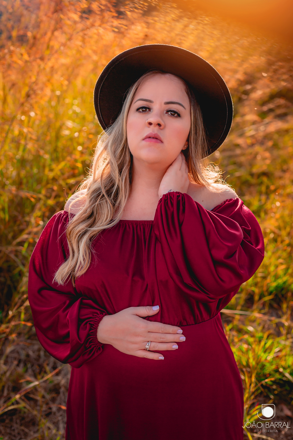 ensaio de mulher gestante em campo aberto com chapéu e vestido vermelho com por do sol