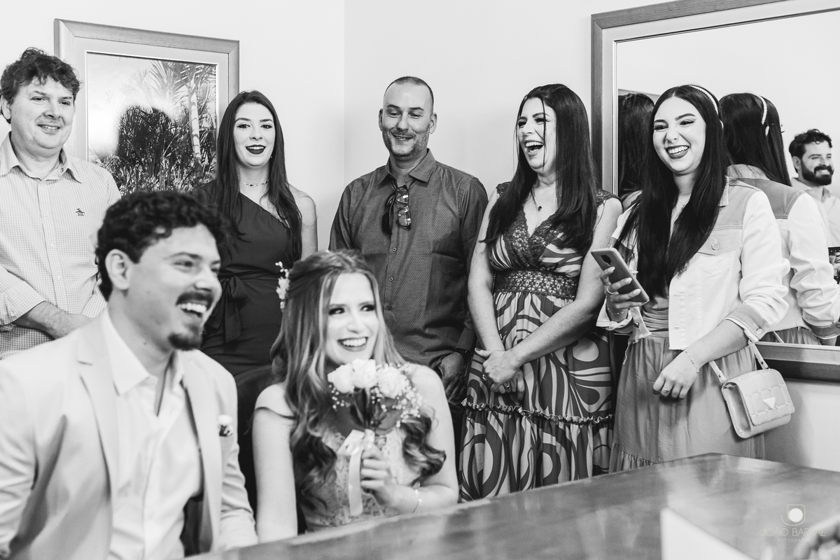 família reunida em cartório rindo em casamento civil com noivos sentados