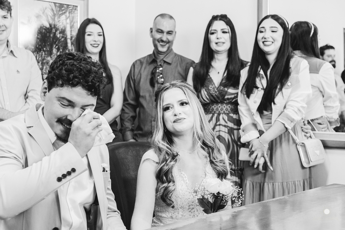 família reunida em cartório rindo em casamento civil com noivos emocionados