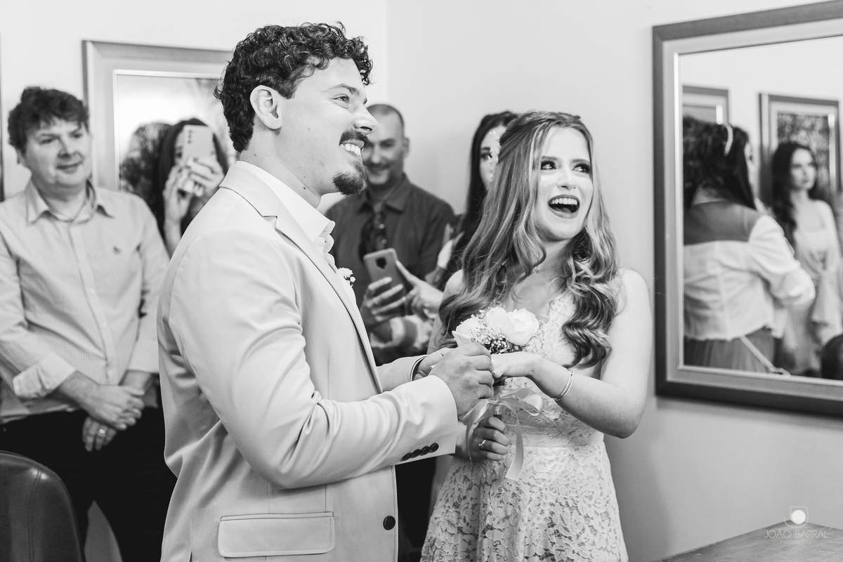 família reunida em cartório rindo em casamento civil com noivos sorrindo no momento das alianças