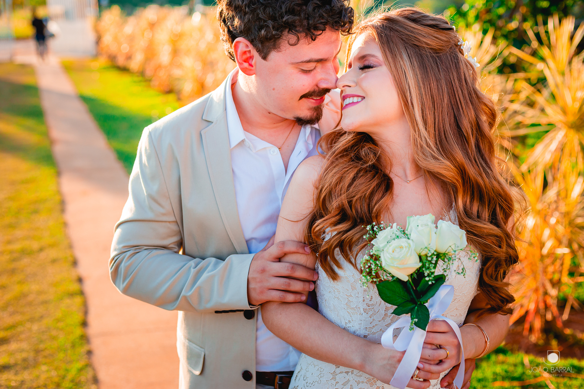 casal de noivos com rosto encostado sorrindo e noiva segurando buque